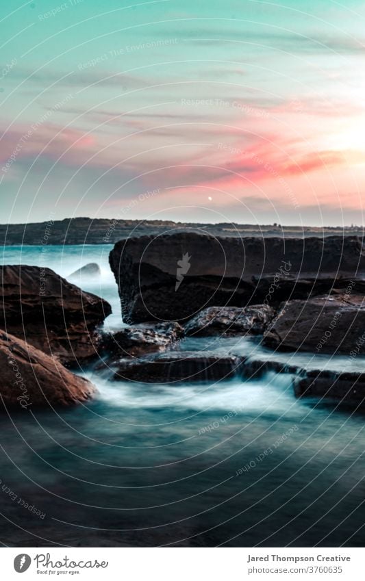 Wellen stürzen bei Sonnenuntergang in Marourbra in Sydney, Australien, über Felsen Meer rosa Frühling nsw newsouthwales Ostküste Strand Steine Sommer blau