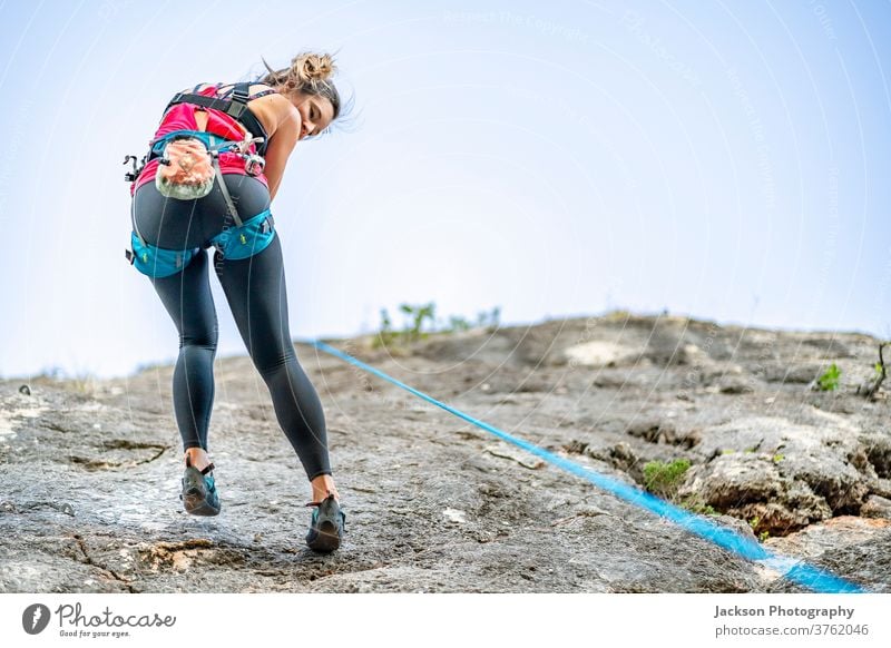 Eine Frau klettert im Klettergurt an einem steilen Felsen Aufsteiger Klettern Kabelbaum nach unten aktiv Aktivität Adrenalin alkoholisch Algarve Klippe Aufstieg