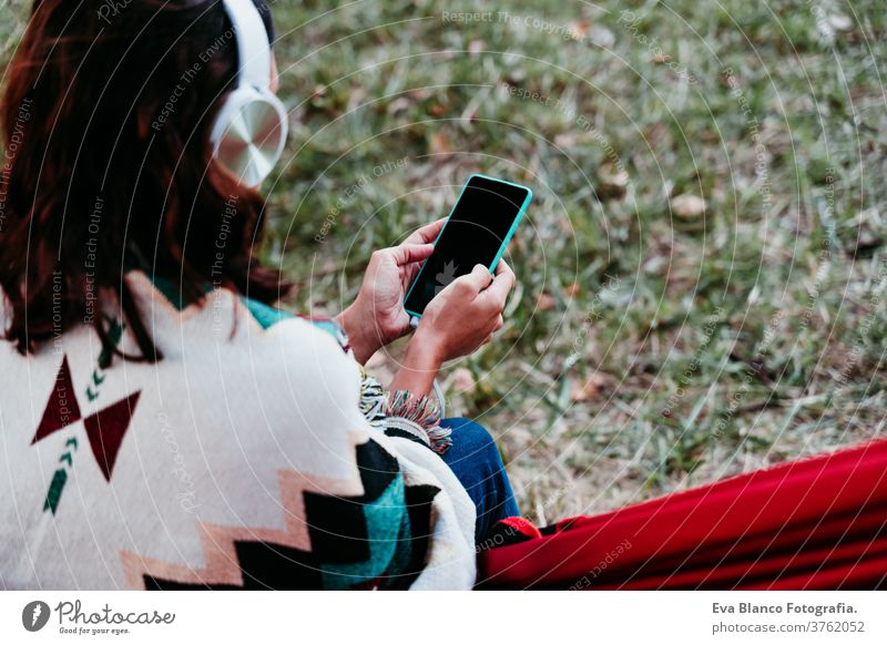 rückansicht einer frau, die sich in der hängematte entspannt und mit handy und headset musik hört. herbstsaison. campingkonzept Headset Kopfhörer hören Musik