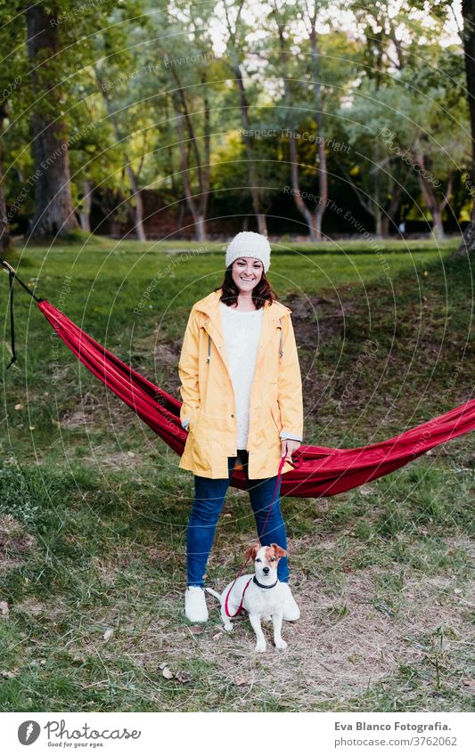 junge frau mit gelbem regenmantel steht neben der hängematte mit ihrem jack russell hund. herbstsaison. camping konzept Frau Hund liegende Hängematte Haustier