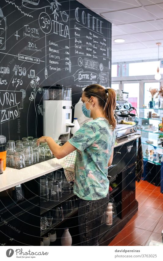 Kellnerin mit Maskenreinigungsbrille Platzierung Reinigen Brille Küchenhandtücher Gesichtsmaske Coronavirus Geschriebene Tafel Kaffeemaschine Überprüfung von