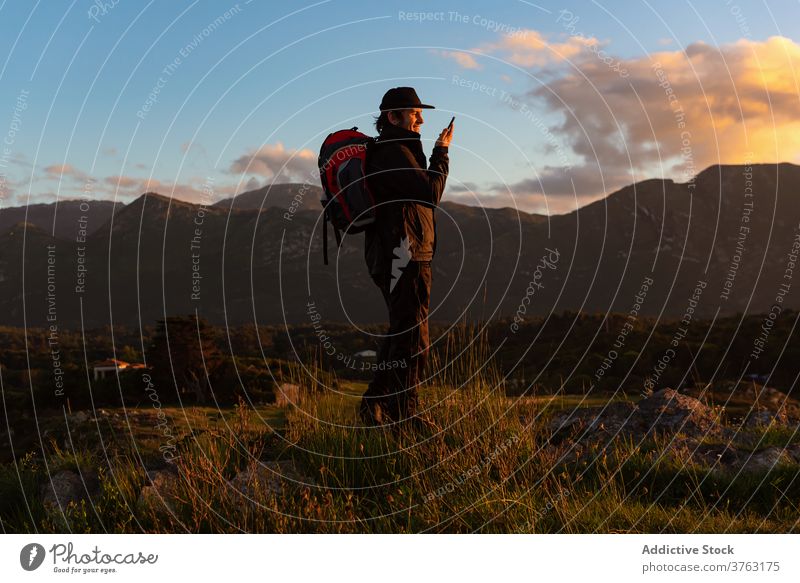 Männlicher Reisender, der in den Bergen mit seinem Smartphone spricht Wanderer sprechen Mann Sonnenuntergang Berge u. Gebirge bewundern benutzend Hochland