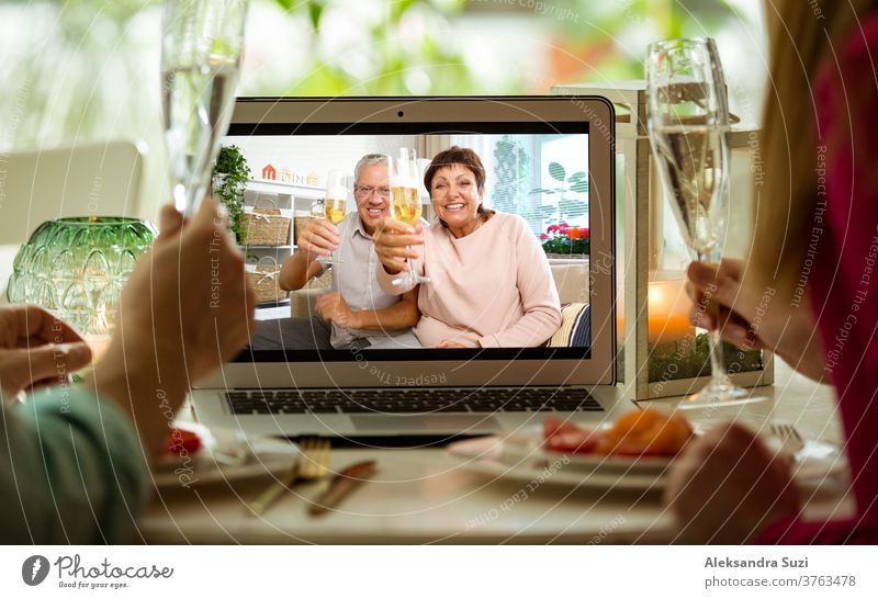 Mann und Frau sitzen am Esstisch, essen zu Abend, trinken Champagner und führen Videogespräche mit älteren Eltern am Laptop. Zu Hause bleiben, Quarantäne und soziale Distanzierung bei der Feier des Ereignisses.