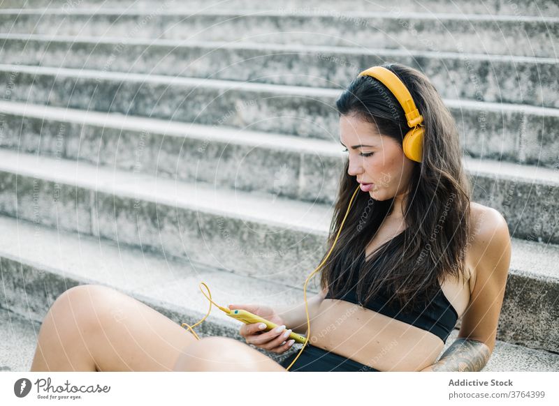 Seriöse Sportlerin beim Musikhören auf der Treppe Smartphone Kopfhörer zuhören ruhen Training Apparatur Athlet Frau benutzend Mobile Telefon Gerät