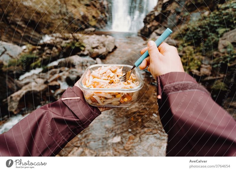 Blickwinkelaufnahme einer Wanderin, die vor einem Wasserfall isst Koch Überleben Picknick gierig Menschen Rucksacktourismus Erholung Menschengruppe Lager Zelt