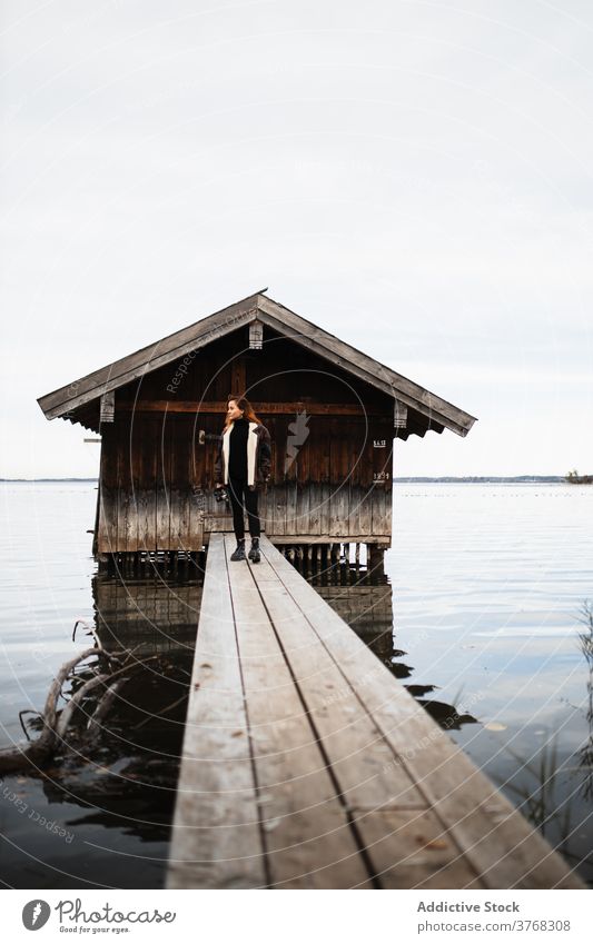 Einsame Frau steht auf Holzsteg am See Pier Baracke Herbst trist einsam Reisender schäbig Windstille ruhig Natur reisen Tourismus Deutschland Österreich hölzern