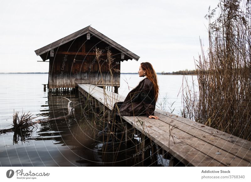 Einsame Frau steht auf Holzsteg am See Pier Baracke Herbst trist einsam Reisender schäbig Windstille ruhig Natur reisen Tourismus Deutschland Österreich hölzern