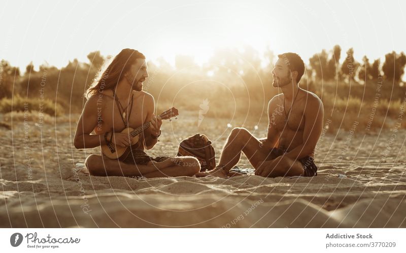 Männliche Freunde spielen Gitarre am Strand Sonnenuntergang Männer Musik Zusammensein sich[Akk] entspannen akustisch zuhören Instrument Hobby sitzen Küste Natur