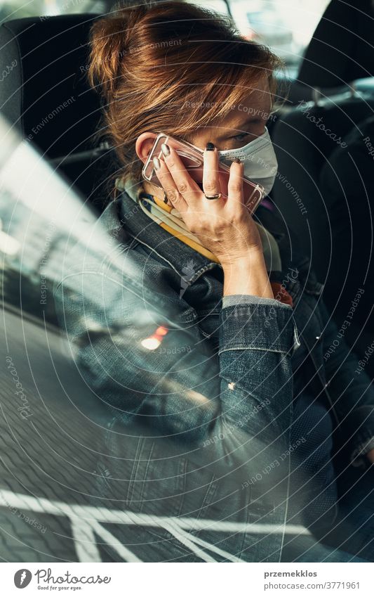 Frau, die mit einem Smartphone telefoniert und mit der Gesichtsmaske in einem Auto sitzt, um eine Virusinfektion zu vermeiden Kaukasier covid-19 Lifestyle