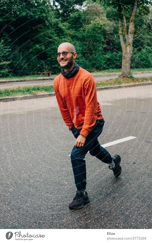 Ein Mann macht Lunges (Ausfallschritte) auf einer Raststätte um sich in der Pause einer Autofahrt etwas zu bewegen Bewegung draußen zwischendurch Straße lächeln