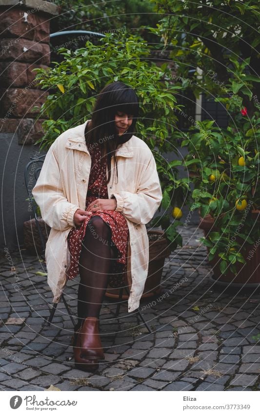 Dunkelhaarige Frau in herbstlicher Kleidung sitzt draußen im Hof auf einem Stuhl und blickt zur Seite dunkelhaarig Herbst langhaarig Blick zur Seite verträumt