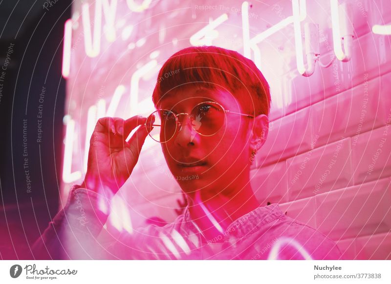 Junger asiatischer Hipster tausendjähriger Mann im Streetstyle-Modekonzept und mit Sonnenbrille in rosa Neonlicht Stilrichtung neonfarbig Jahrtausende gen z