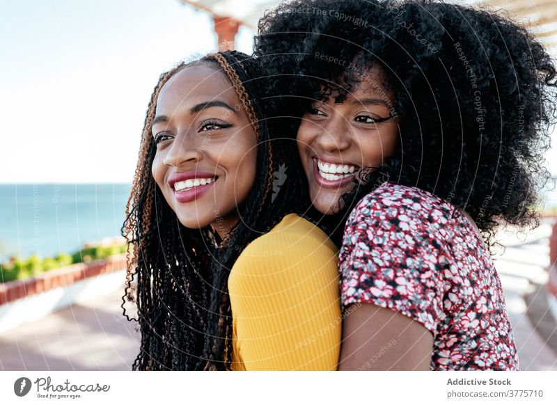 Fröhliche ethnische Frauen, die sich an der Strandpromenade umarmen bester Freund Umarmung Freundschaft Zusammensein Freude Sommer Stauanlage schwarz