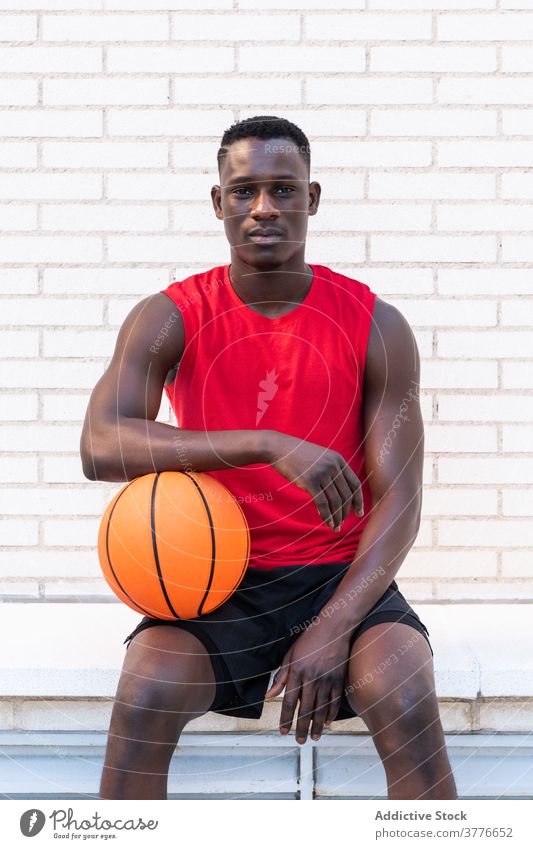 Ernster ethnischer Mann mit Basketball auf dem Platz Spieler Ball sich[Akk] entspannen Sportler Sportpark Spielplatz Stein Borte Bestimmen Sie männlich schwarz