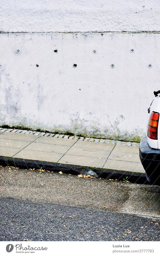 leuchtend rot - ein einsames Rücklicht bzw. das Heck eines alten Autos am Straßenrand, dazu Regen und grau Bürgersteig knallrot Stoßstange Wand Fassade