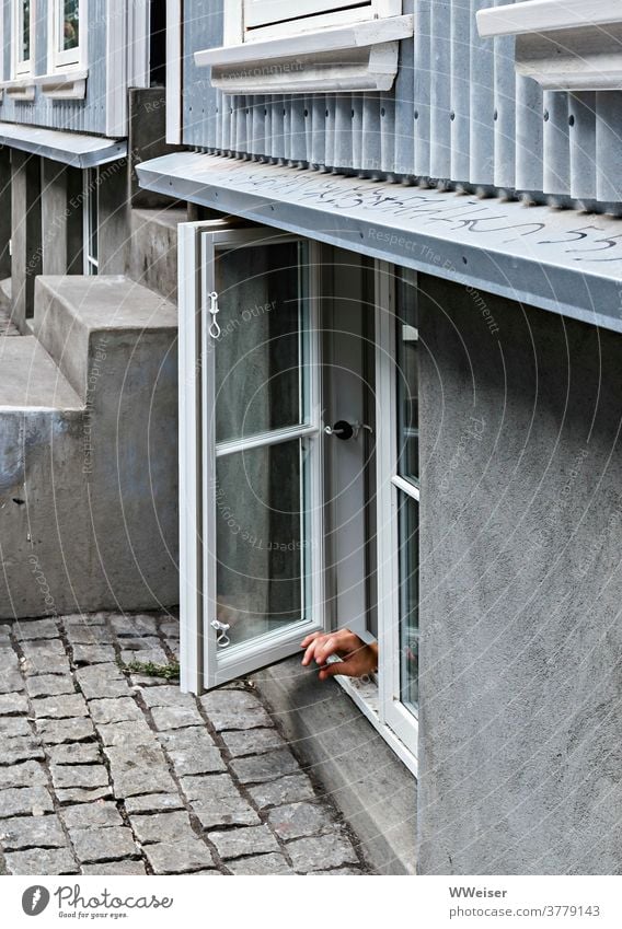 Eine Hand ragt mit unklarer Geste aus dem offenen Fenster im Souterrain Finger zeigen rauchen Handzeichen Fensterrahmen Erdgeschoss Parterre Treppe Sockel Haus