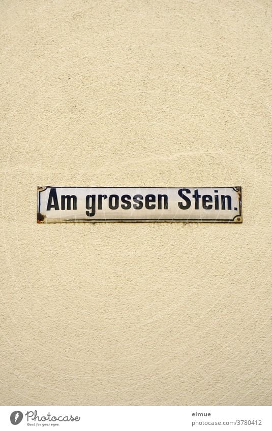 Straßenschild "Am großen Stein" an einer beigefarbenen Hauswand Straßenname Schild Wand Fassade Schrift Hinweisschild Adresse wohnen alt Putz