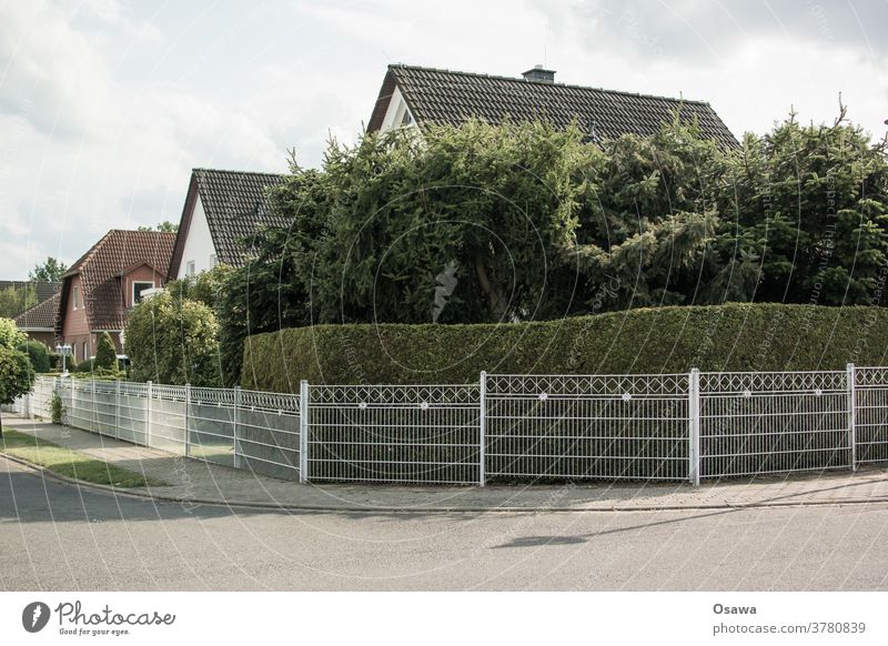 Einfriedung mit Eigenheim Eigenheimidyll Eigenheimsiedlung Haus Dach Satteldach Krüppelwalm Zaun Grenze Hecke Einsiedlerkolonie Außenaufnahme Menschenleer