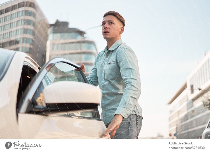 Ernster Mann steigt in Auto in Stadt ein PKW Automobil einsteigen geparkt Straße Großstadt Fahrer männlich modern urban gutaussehend Fahrzeug Verkehr parken