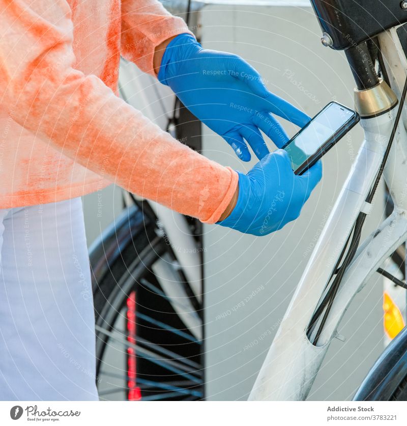 Crop-Frau mit Smartphone mietet Fahrrad während Pandemie Miete benutzend Station App Handschuh Straße Großstadt Madrid Spanien Latex Seuche Gerät Apparatur