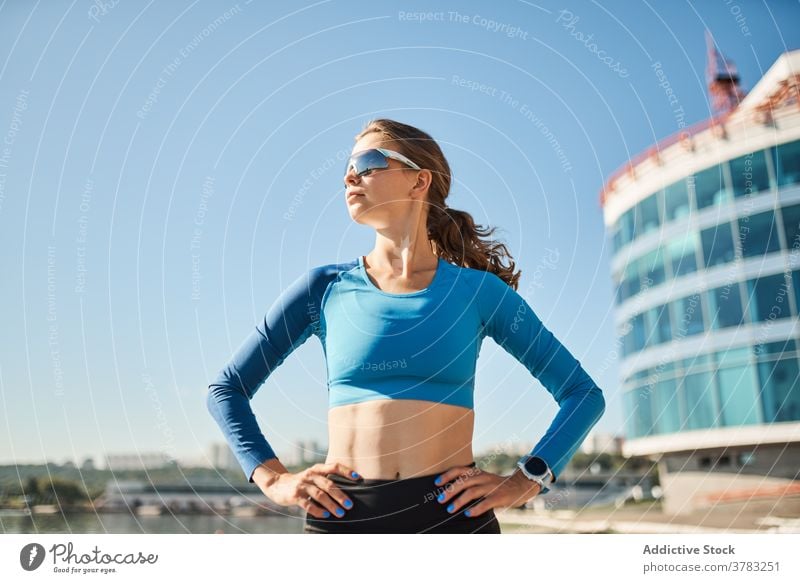 Schlanke aktive Frau in Sportkleidung und Sonnenbrille steht in der Nähe von Fluss sportlich selbstbewusst passen schlank Training Fitness Tracker