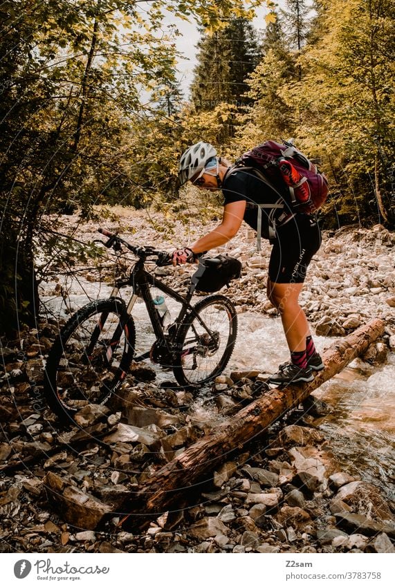 Junge Frau überquert Fluß Bach mit ihrem Mountainbike mountainbike mtb fahrrad abenteuer bach fluss überqueren schieben steine wald alpen berge natur landschaft