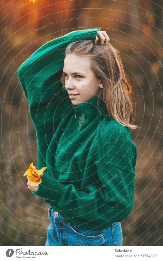 Porträt eines schönen Teenagermädchens mit blonden Haaren und blauen Augen mit einem Lächeln im Gesicht und einem herbstlich gelben Blatt im Park. Herbst Glück