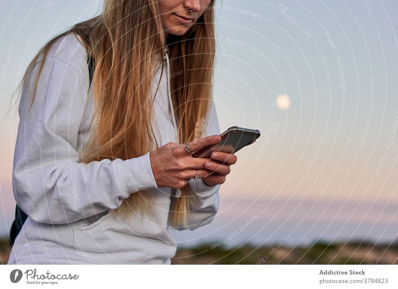 Friedliche Frau, die auf der Promenade bei Sonnenuntergang auf ihrem Smartphone surft Spazierweg reisen Browsen benutzend Dämmerung sich[Akk] entspannen