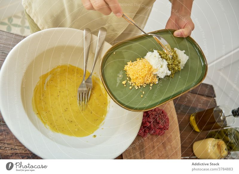 Crop Koch Kochen Steak Tartar in der Küche Senf Küchenchef Saucen Speise hinzufügen Zitrone Schale Anchovis Eigelb Zwiebel Kapriolen Rezept eingießen