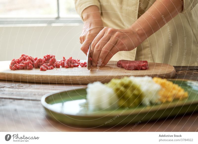 Crop Frau Schneiden von Fleisch in der Küche geschnitten Rindfleisch Koch Steak Tartar Hausfrau vorbereiten Abendessen Speise Schneidebrett frisch hölzern