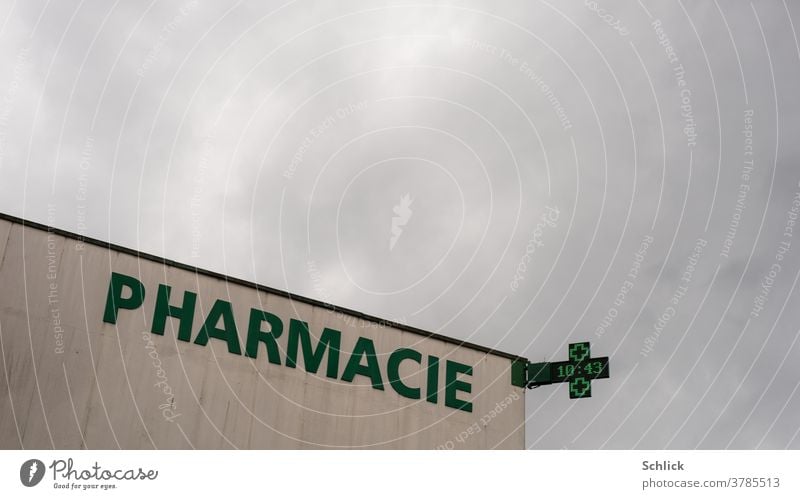 Apotheke in Lothringen mit Schriftzug Pharmacie und Leuchtreklame mit Uhrzeit viel bedeckter Himmel Frankreich grün modern Kreuz Beton Betonwand