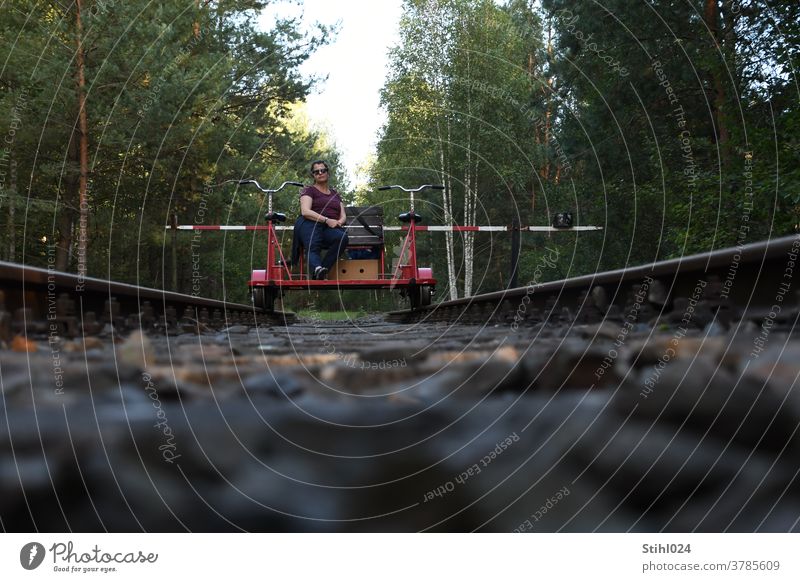 Pause machen auf der Draisine Fahrraddraisine BAhnstrecke Gleis Schotterbett Wald Schranke rot-weiß sitzen erholen Fitness Froschperspektive geradeaus vorwärts