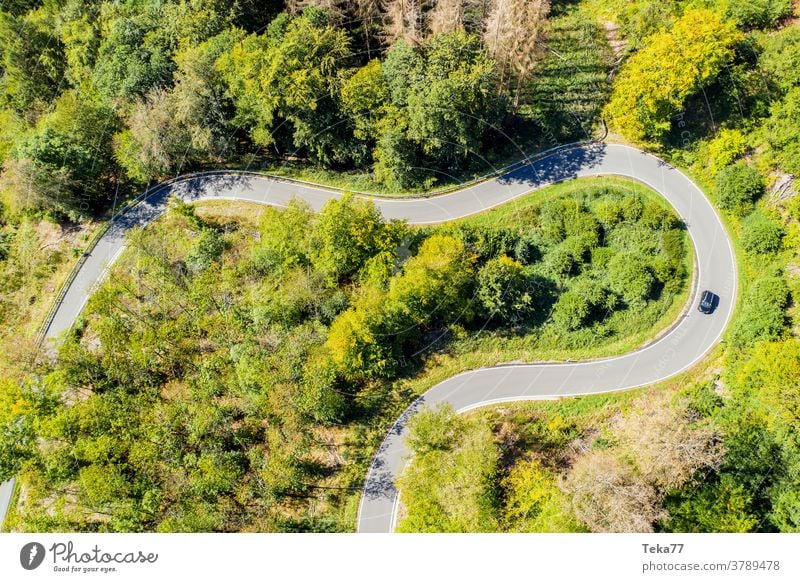 ein Auto auf einer kurvigen Forststraße von oben PKW Auto von oben Forstweg Wald Wald von oben Straße von oben Beton Sommer Landschaft Transport Sonne Schatten