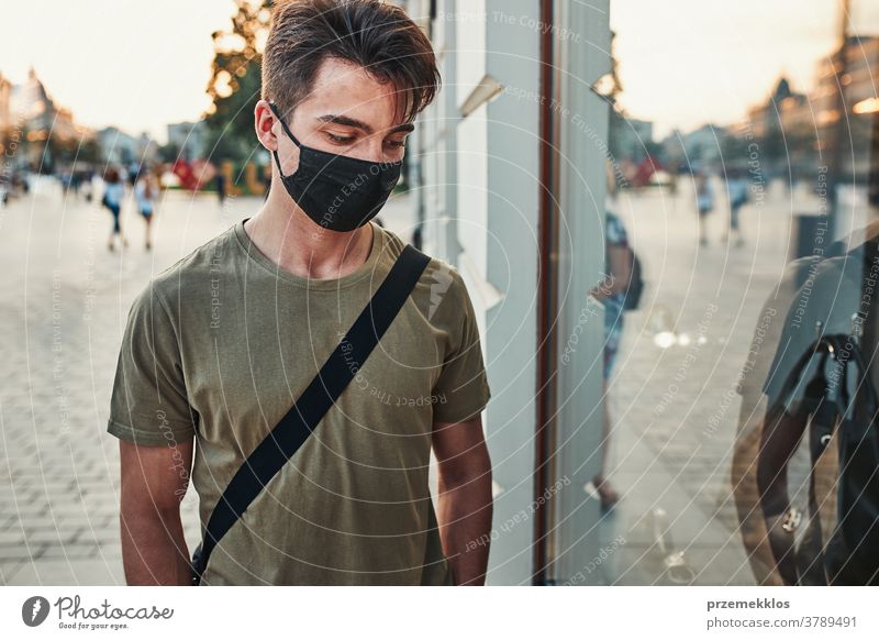 Junger Mann geht an einer Ladenfront im Stadtzentrum entlang und trägt die Gesichtsmaske, um eine Virusinfektion zu vermeiden Kaukasier Gespräch covid-19