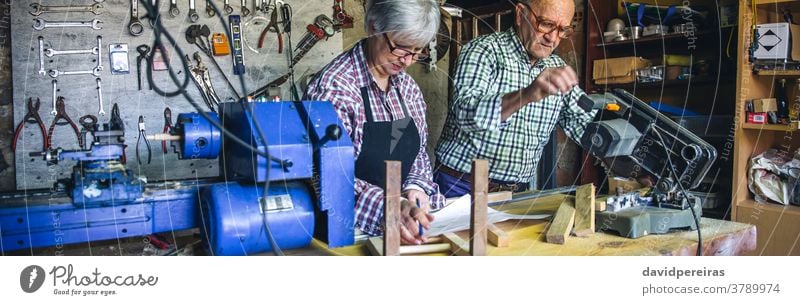 Seniorenpaar in einer Tischlerei Zimmerer Gehrung benutzend Schreinerei Paar arbeiten Blick plant Werkstatt Transparente Panorama panoramisch Netz Holz reif