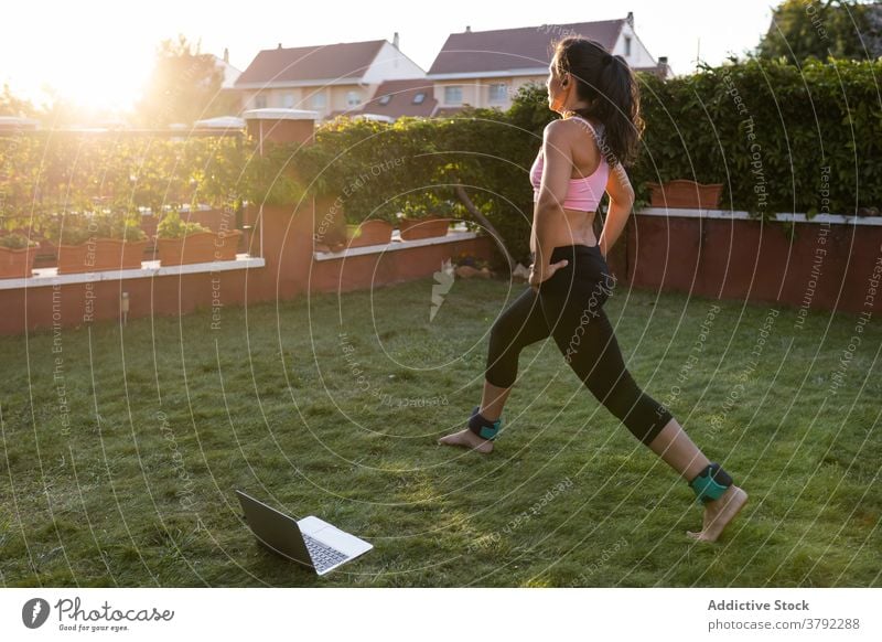 Schlanke Frau macht Übungen im Innenhof im Sommer Ausfallschritt Training Laptop online Tutorial benutzend Athlet Sonnenuntergang Sportbekleidung Gesundheit