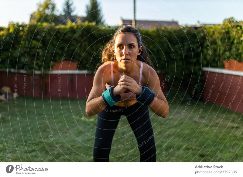 Schlanke Frau macht Übungen im Innenhof im Sommer Training Kniebeuge Laptop online Tutorial benutzend Athlet Sonnenuntergang Sportbekleidung Gesundheit Fitness