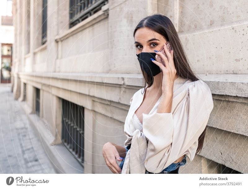 Trendy Frau in Maske sprechen auf Handy auf der Straße reden Smartphone Coronavirus Mundschutz behüten benutzend Stil Stein Gebäude Großstadt Gespräch Anschluss