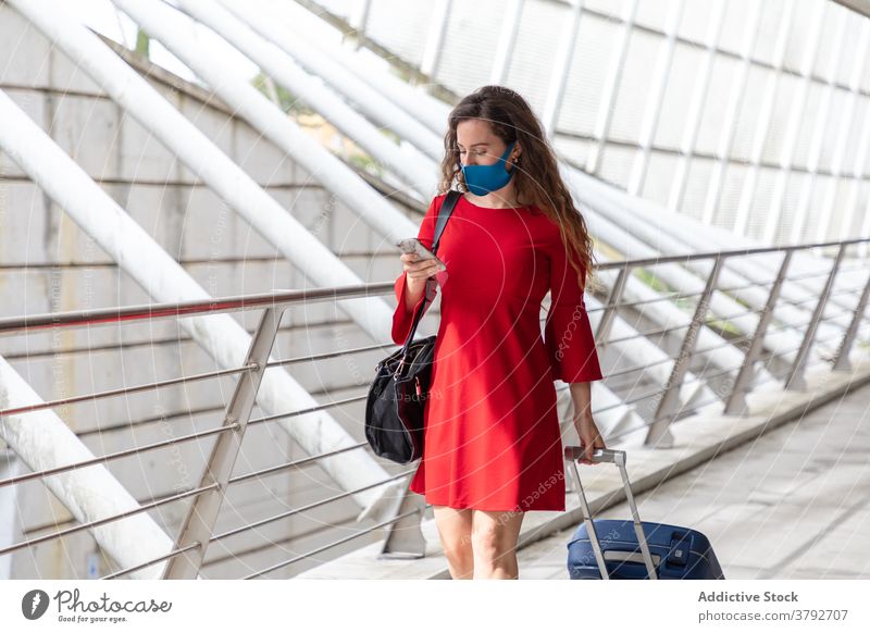 Reisende Frau mit Koffer im Flughafen Tourist Mundschutz Coronavirus Gepäck Smartphone benutzend Saal Abheben Pandemie reisen Ausflug Gerät warten Apparatur