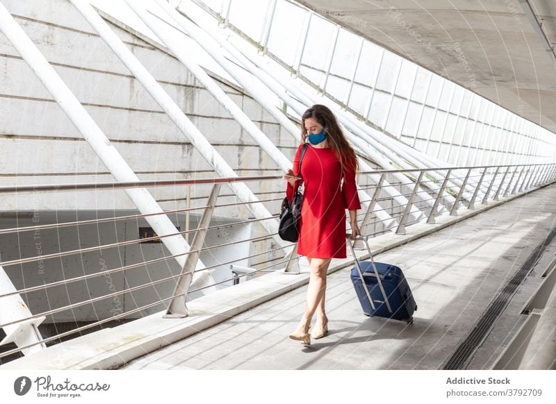 Reisende Frau mit Koffer im Flughafen Tourist Mundschutz Coronavirus Gepäck Smartphone benutzend Saal Abheben Pandemie reisen Ausflug Gerät warten Apparatur