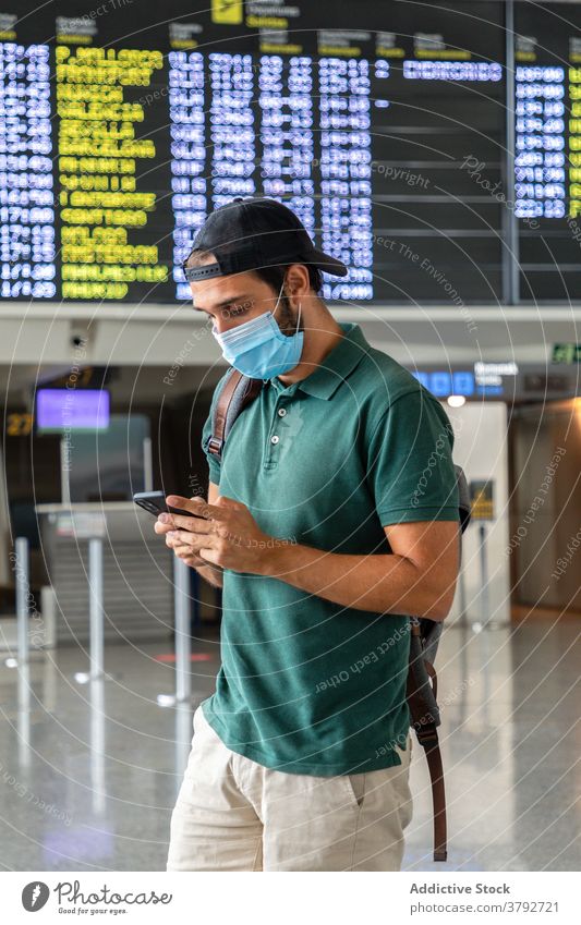 Reisender in Maske mit Handy im Flughafen warten Mann Abheben Terminal Holzplatte Smartphone benutzend Mundschutz männlich Bund 19 Passagier modern Browsen