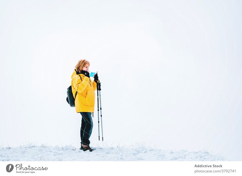 Wanderer mit Schutzmaske auf verschneitem Gelände stehend Trekking Reisender Mundschutz Coronavirus aktiv Schnee Berge u. Gebirge Rucksack Abenteuer COVID19