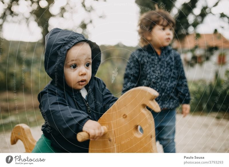 Kind auf hölzernem Schaukelpferd Geschwister Hermandad Holzpferd Herbst Pferd Kindheit Farbfoto Spielen Außenaufnahme Freude Spielzeug Tag Spielplatz