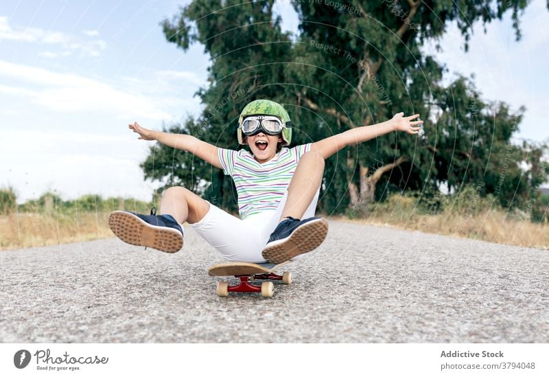 Glücklicher Junge auf Skateboard in Schutzbrille Schutzhelm Spaß haben sorgenfrei Kindheit aufgeregt Inhalt Straße stylisch Bekleidung Brille dekorativ Sommer