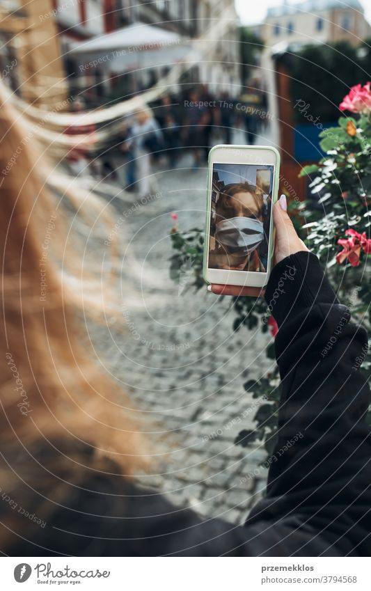 Junge Frau mit Videogesprächen, die abends auf einem Spaziergang durch die Innenstadt mit der Gesichtsmaske spricht, um eine Virusinfektion zu vermeiden Anruf