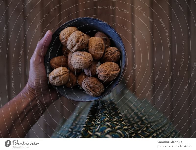 Frau in einem grün gemusterten Kleid auf einem Holzboden stehend, hält eine Schale voller Walnüsse in der Hand Nüsse blau Muster Herbst Frucht Essen rustikal