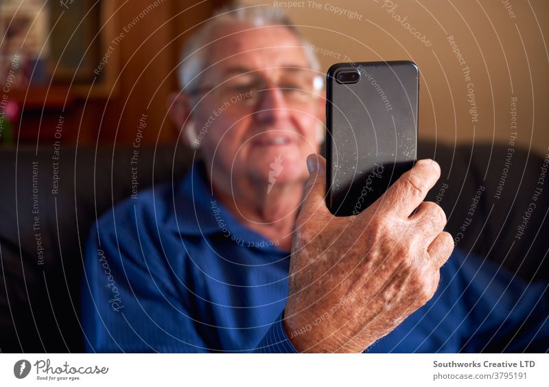 Lächelnder älterer Mann zu Hause macht Videoanruf an Familie auf Mobiltelefon Senior Senioren Video-Chat Mobile Handy Zelle verbunden online Technologie