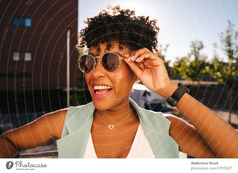 Stilvolle ethnische Frau mit Sonnenbrille in der Nähe von Zaun stehen trendy Glück Sommer Afro-Look Lächeln heiter jung Afroamerikaner schwarz positiv