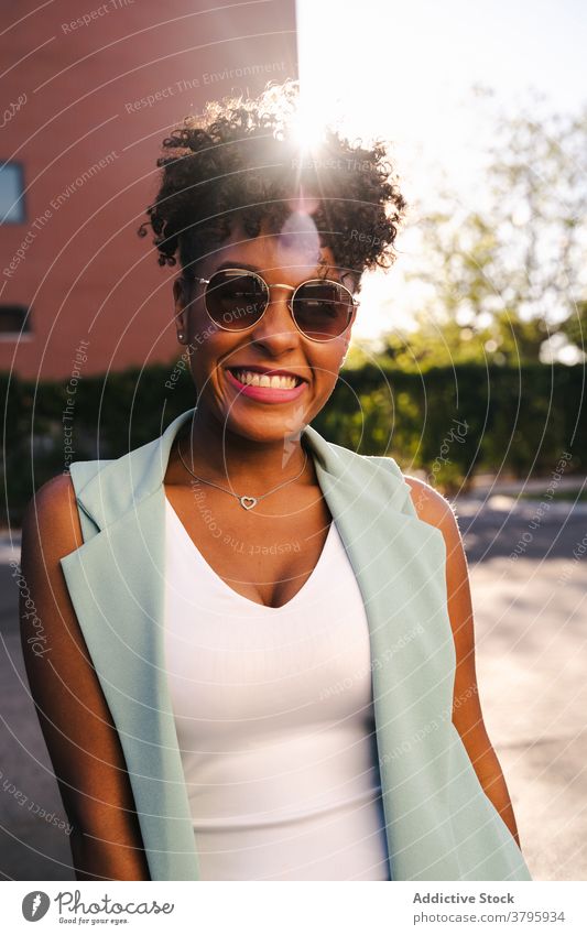 Stilvolle ethnische Frau mit Sonnenbrille in der Nähe von Zaun stehen trendy Glück Sommer Afro-Look Lächeln heiter jung Afroamerikaner schwarz positiv