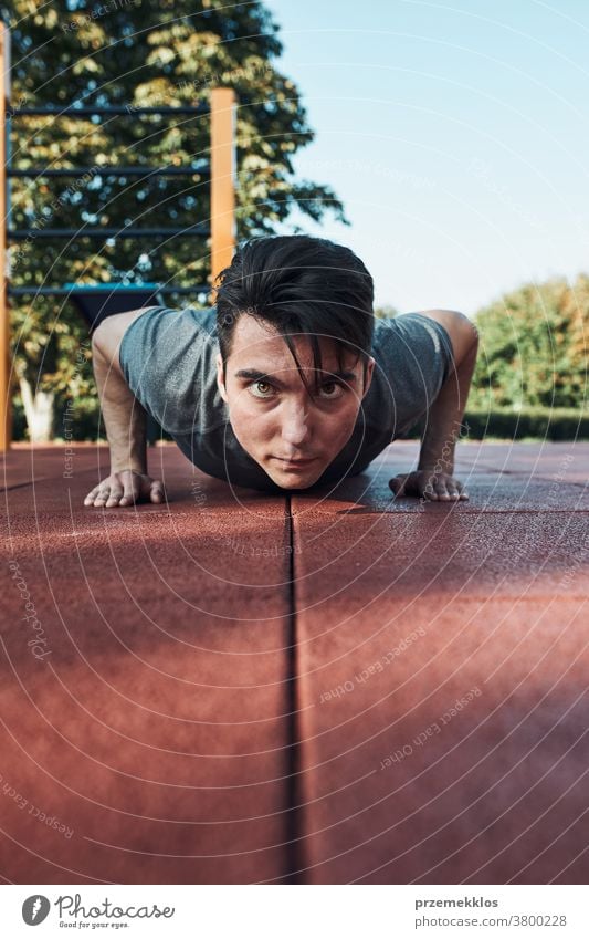 Junger Mann macht Liegestütze auf rotem Gummiboden während seines Trainings in einem modernen Trainingspark für Gymnastik calisthenics Pflege Kaukasier